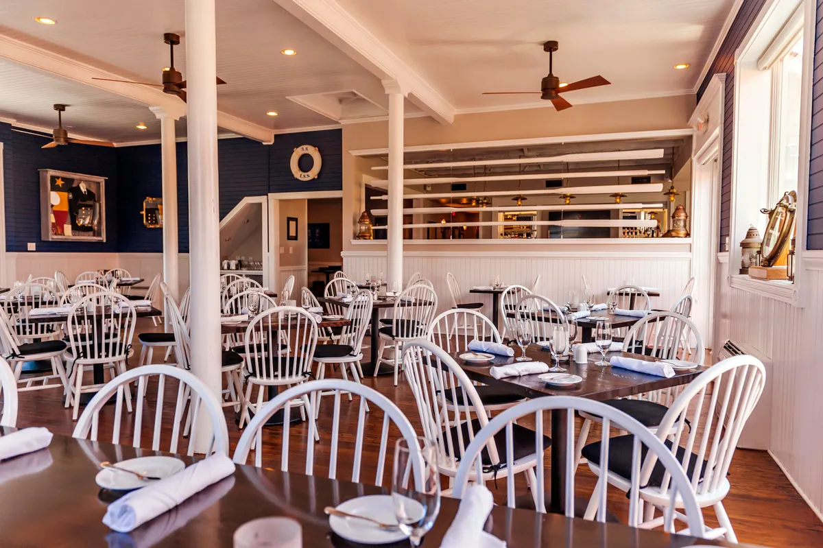 This image features a bright, welcoming dining area with white wooden chairs, dark wooden tables, and decorative wall art. The setup suggests a casual, friendly atmosphere ideal for families and groups to enjoy shared meals. The space feels open and lively, capturing the essence of relaxed dining within the resort.