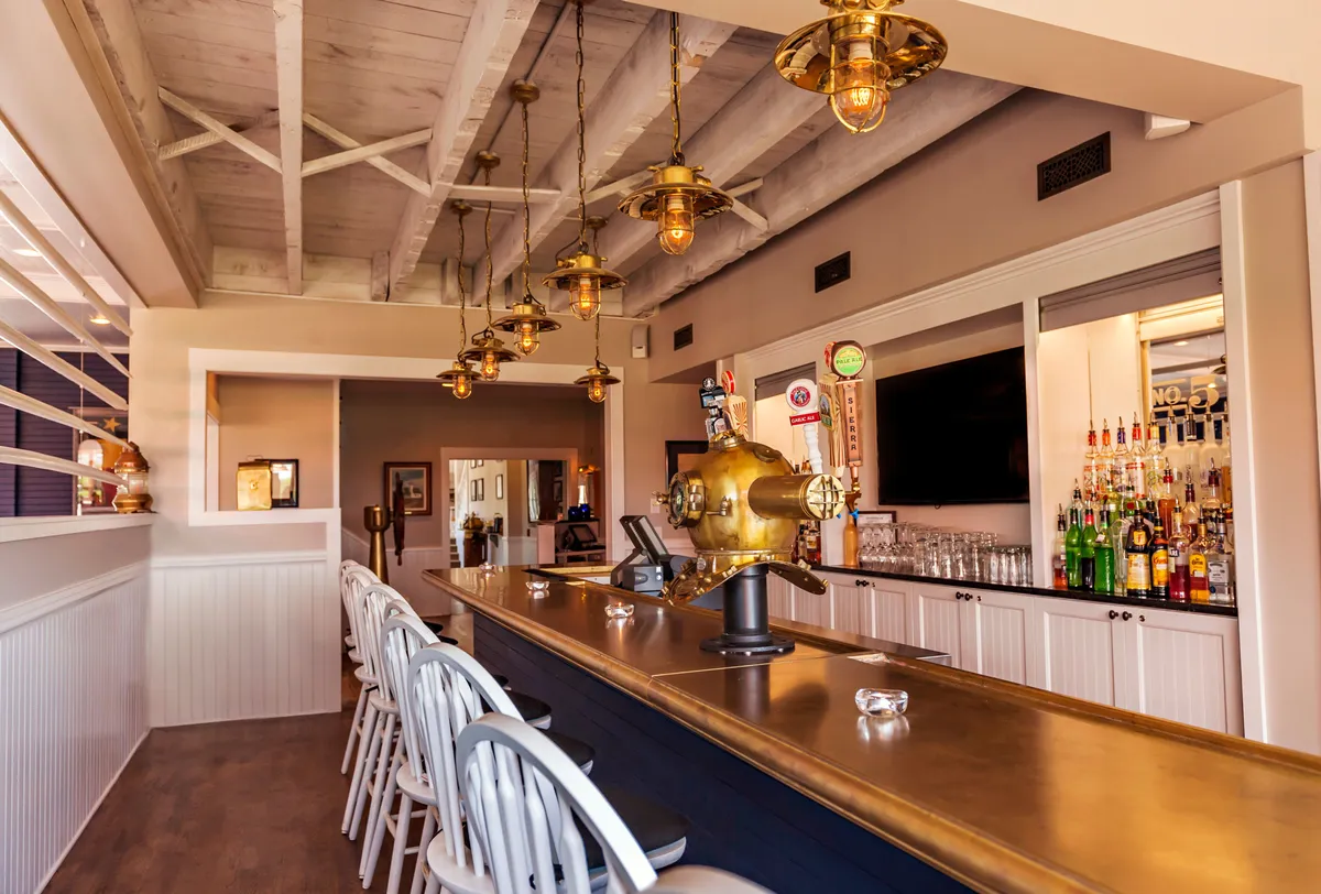 A stylish interior bar scene with a well-lit counter, decorative shelving filled with bottles, and inviting seating. The setting is designed for social interaction, with guests enjoying drinks and lively conversation in a relaxed yet energetic atmosphere.