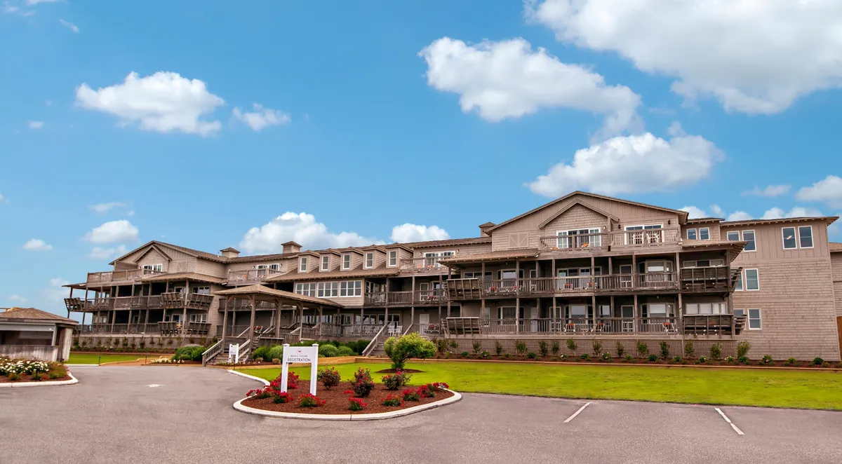 This image captures the exterior facade of the building, prominently featuring multiple balconies overlooking landscaped gardens. The scene is tranquil and welcoming, with sunlight illuminating the balconies—hinting at the private outdoor spaces available to guests. The view suggests the potential for memorable sunset views from these balconies.
