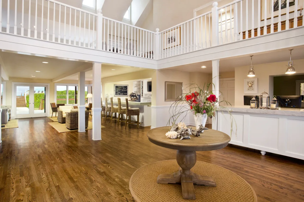 A bright, cheerful interior scene with a central round table decorated with fresh flowers, an open kitchen in the background, and large windows flooding the space with light and offering views to the outdoors. The setting is perfect for gathering, planning outings, or sharing stories after a day of adventure.